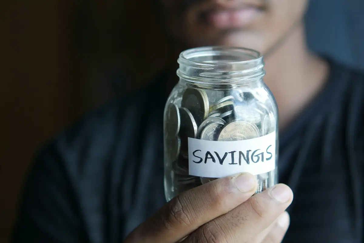 Person putting coins into a savings jar, representing a buyer building toward a home loan deposit