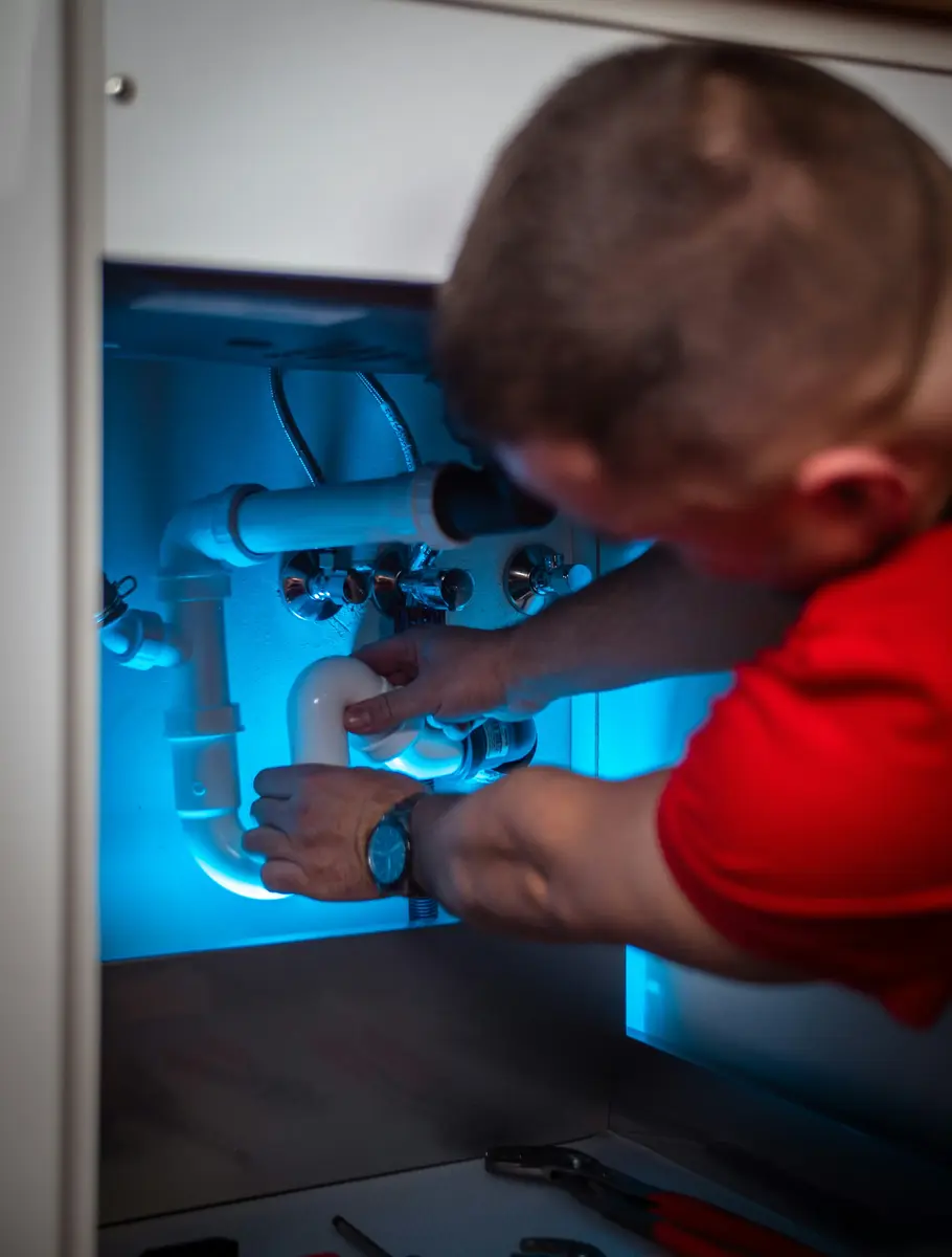 A plumber working on a pipe inside a cabinet, the kind of careful, licensed work that builds a plumbing business's reputation