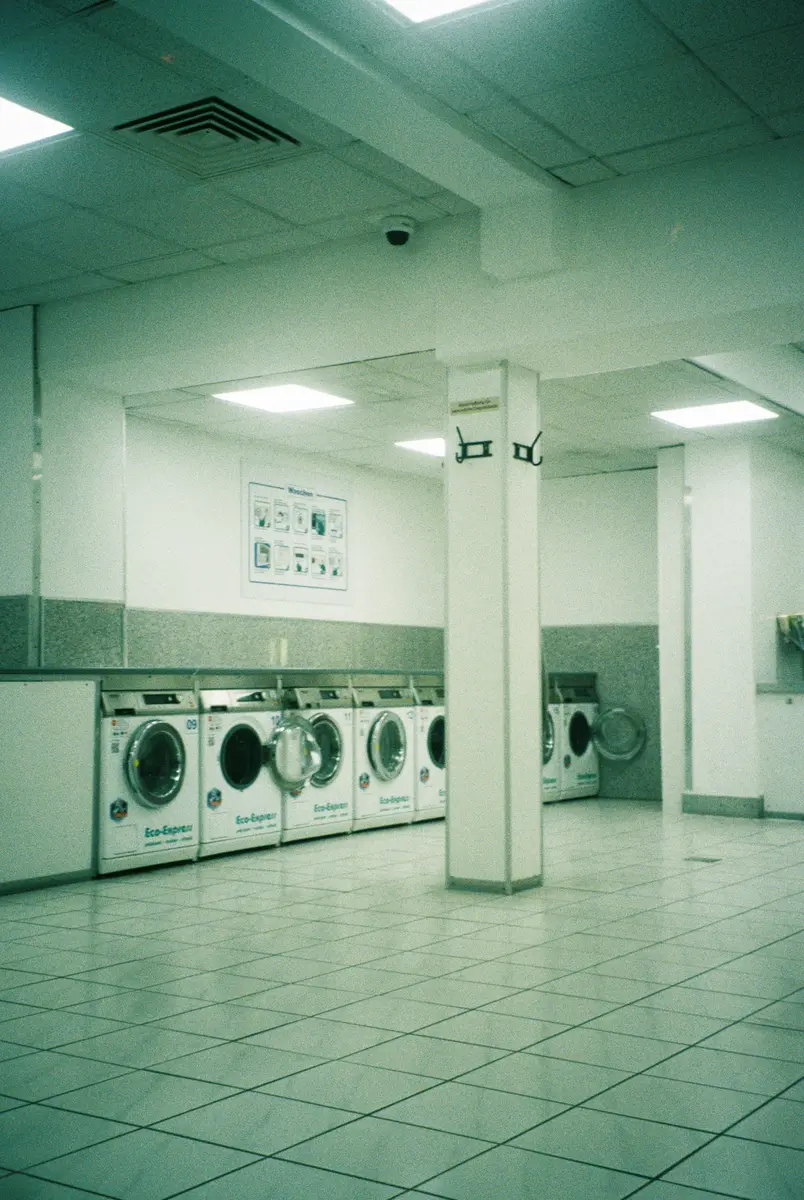 A row of washing machines in a brightly lit laundromat, the kind of space a laundry business needs to keep full